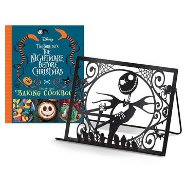The image shows the cover of a cookbook titled 'Tim Burton's The Nightmare Before Christmas: The Official Baking Cookbook' featuring colorful illustrations of characters from the movie. There is also an exclusive metal cookbook/tablet stand with a Nightmare Before Christmas design.